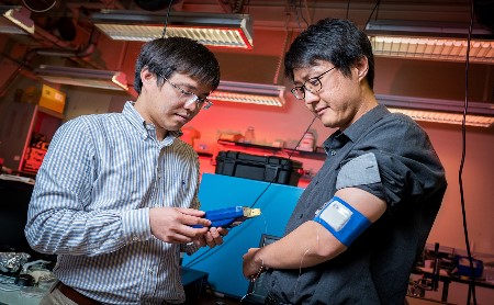 Renkun Chen (left), UC San Diego professor of mechanical and aerospace engineering, measures the temperature of the prototype cooling/heating system worn by Sahngki Hong (right), the study's first author. Source: UC San Diego