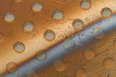 Circles appear on a graphene sheet where the sheet is draped over an array of round posts, creating stresses that will cause these discs to separate from the sheet. The gray bar across the sheet is liquid being used to lift the discs from the surface. Source: Felice Frankel