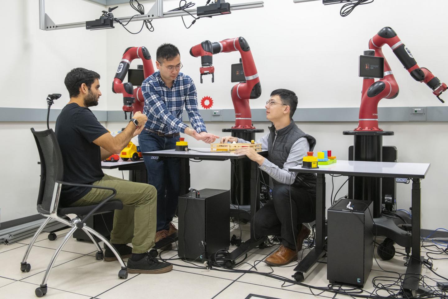 Using a handheld device, Ajay Mandelkar, Jim Fan and Yuke Zhu use their software to control a robot arm. Source: L.A. Cicero