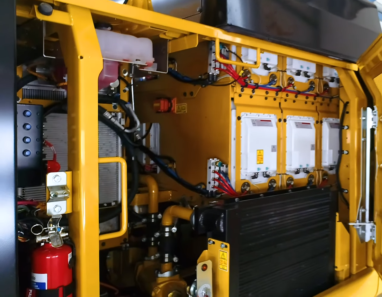 Behind the hatch of the Cat 323F Z-line on the same side of the vehicle as the cabin entrance. A stack of batteries is mounted above a heat exchanger for the hydraulic system. Source: Pon Cat
