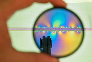 A tabletop simulator is viewed through a polarized camera lens. Photo-elastic plates reveal discrete points of stress buildup along both sides of the modeled fault as the far (upper) plate is moved laterally along the fault. (Source: Los Alamos National Laboratory)