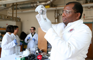 ISU Assistant Professor Martin Thuo holds a vial of liquid-metal particles. Working behind him are (l-r) Simge Cinar, Jiahao Chen and Ian Tevis. Image credit: Christopher Gannon.