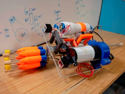 This view of the robot shows the eight orange spear tips mounted on the blue carousel, two small boxes just behind the carousel containing cameras, the electronics chamber behind the right camera, and the buoyancy chamber behind the left camera. Source: WPI