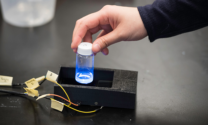 A vial containing quinine solution fluoresces during the testing of a portable diabetes screening device. The small black box is designed to screen for risks of diabetes without using blood samples, and can work in remote areas without refrigeration, power or cell service. Source: University of Rochester / J. Adam Fenster