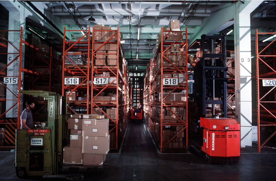 Workers using computerized forklifts in an automated warehouse. Source: Public domain